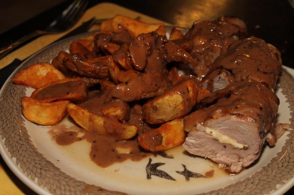Schweizer Schweinefilet mit Kartoffelspalten und Soße auf dem Teller